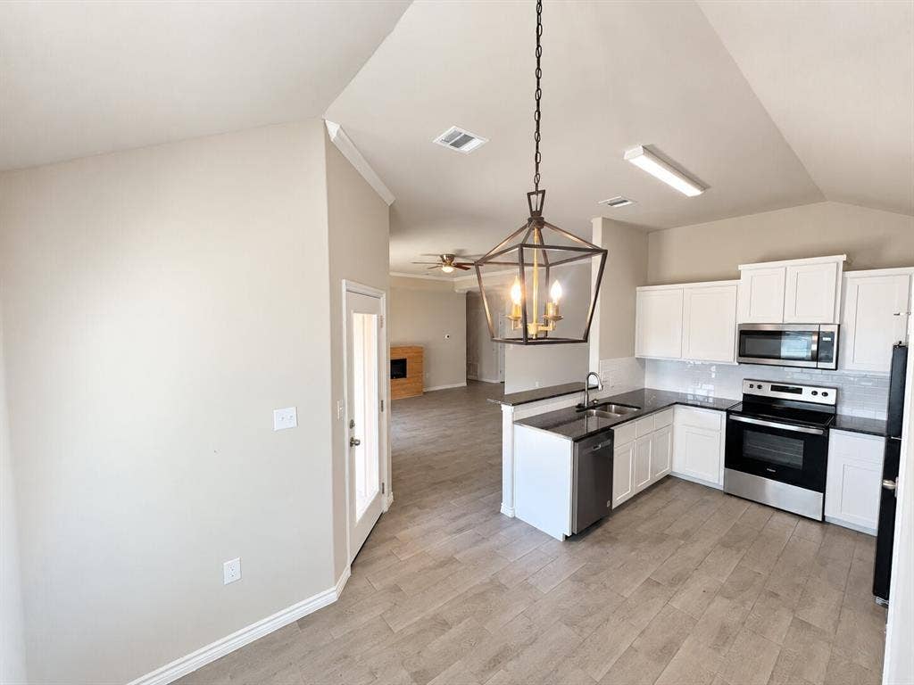 1306 Campbelton Drive, Temple, TX 76504 Vaulted ceilings, wood-finish flooring, white shaker-style cabinetry, black stone-finish countertops, and a metallic geometric pendant light fixture