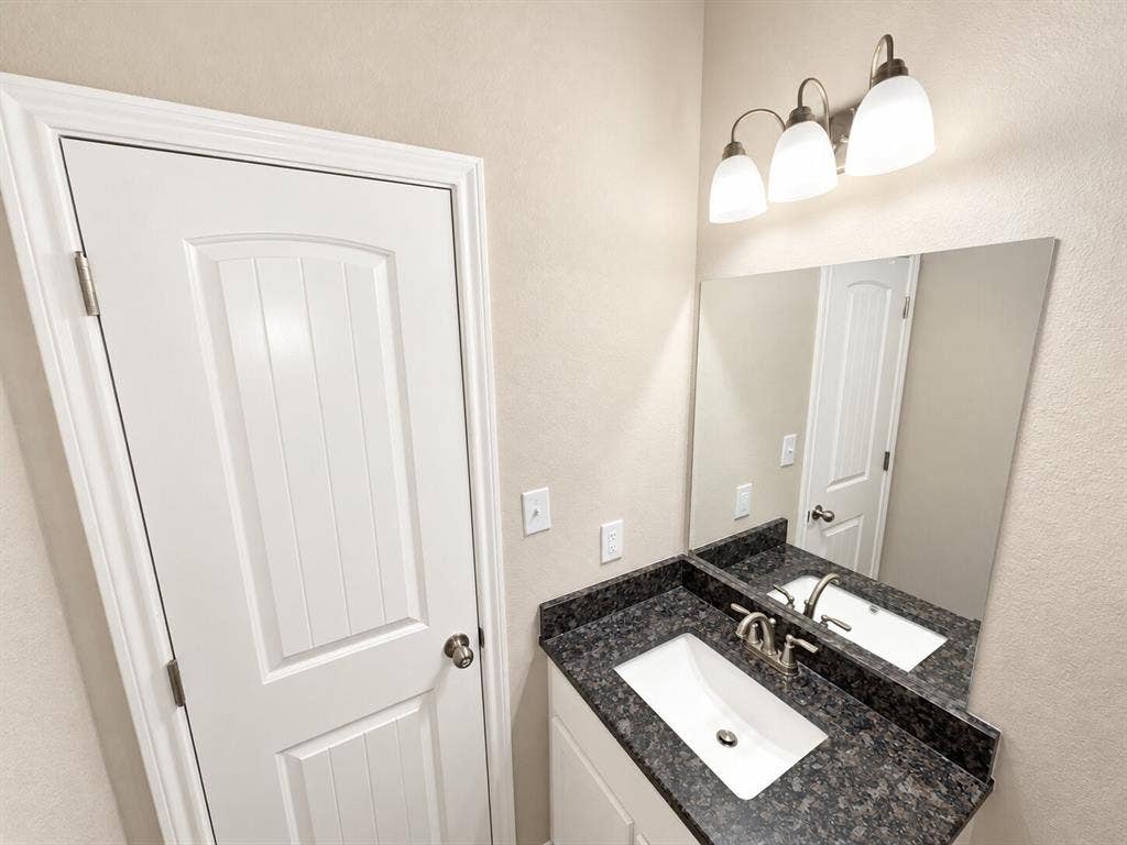 1306 Campbelton Drive, Temple, TX 76504 Vanity featuring a dark stone-finish countertop, white under-mount sink, chrome faucet, three-light wall fixture, and large wall-mounted mirror