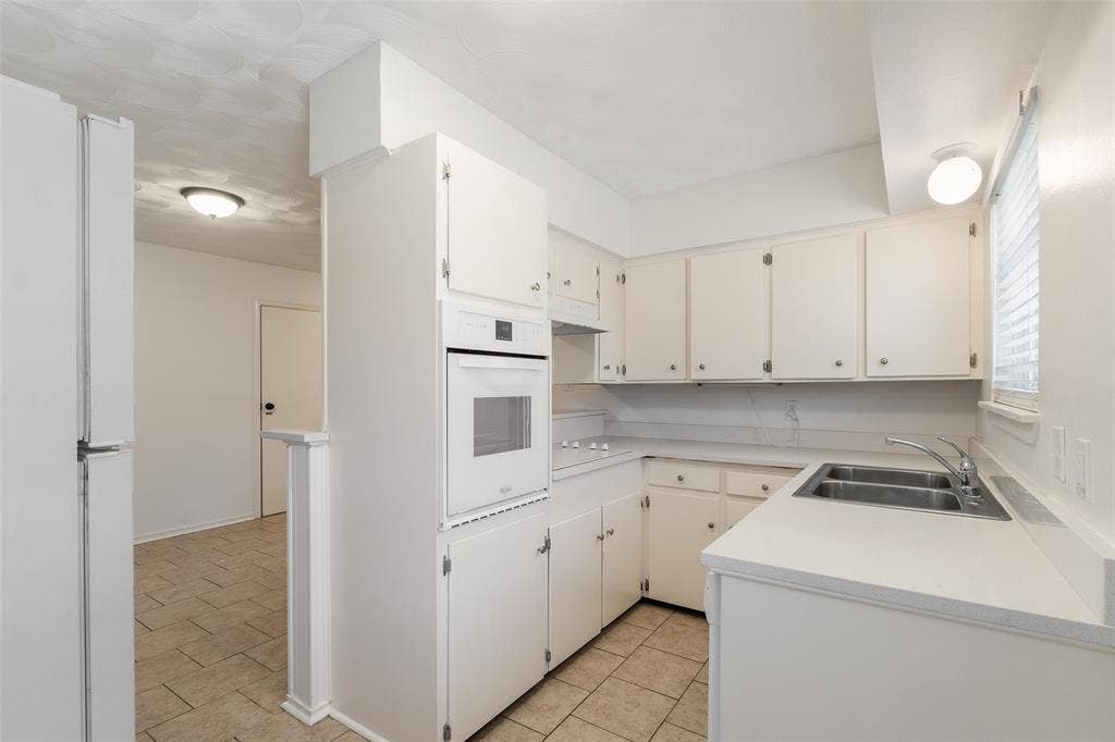 11038 Wyatt, Dallas, TX 75218 Kitchen featuring solid-surface countertops, dual-basin stainless steel sink, built-in wall oven, flush-mount lighting, and tile flooring
