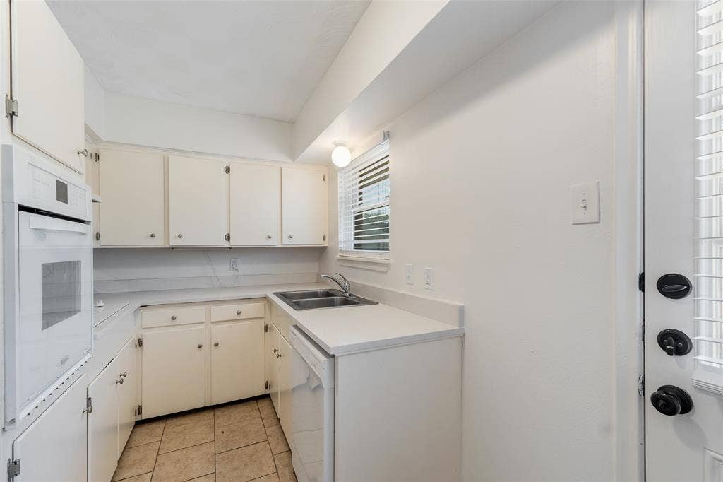 11038 Wyatt, Dallas, TX 75218 Kitchen featuring white cabinetry, solid-surface countertops, dual-basin stainless steel sink, built-in wall oven, and ceramic tile flooring