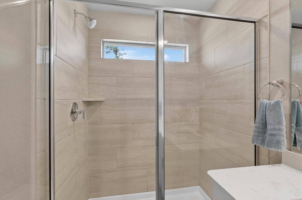 903 Edgehurst Drive, Princeton, TX 75071 Glass-enclosed shower with full-height tiled walls, an integrated shelf, and a transom window