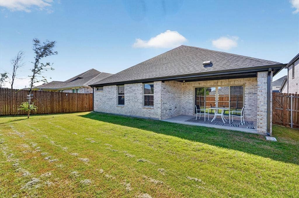 903 Edgehurst Drive, Princeton, TX 75071 Expansive backyard featuring a covered patio, sliding glass door access, white brick exterior, and a wood privacy fence