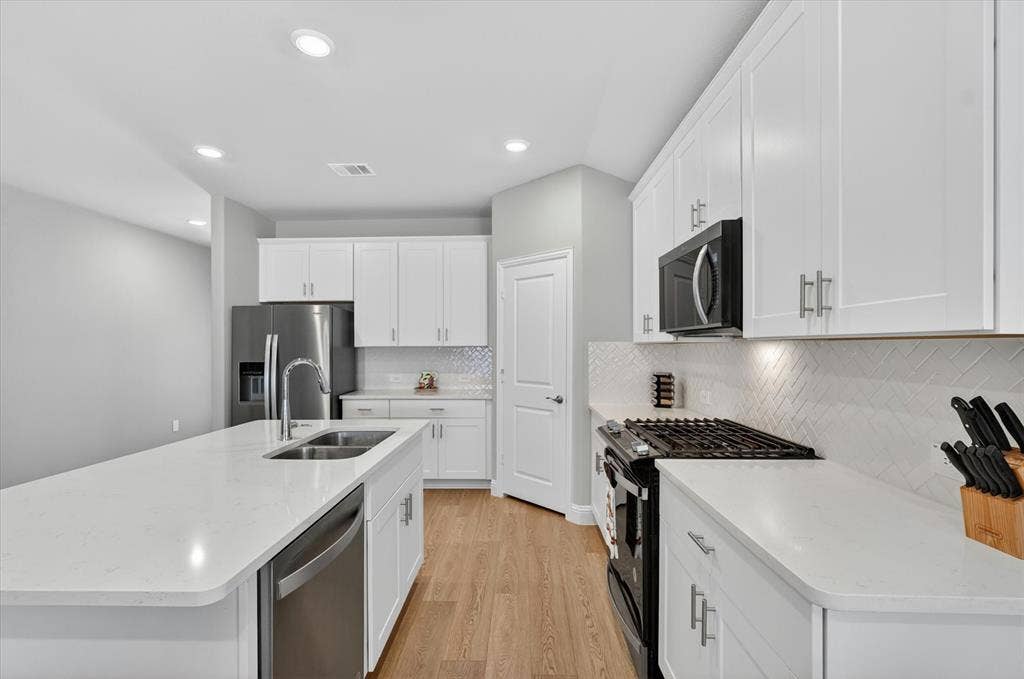 903 Edgehurst Drive, Princeton, TX 75071 Modern kitchen featuring a large island with an undermount sink, white shaker cabinetry, stainless steel appliances, and wood-finish flooring