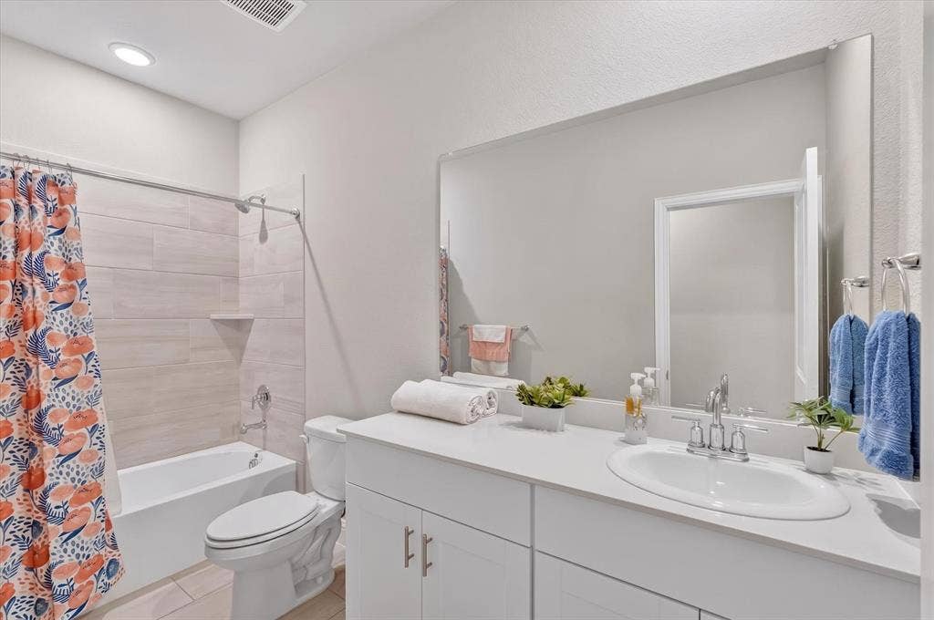 903 Edgehurst Drive, Princeton, TX 75071 Bathroom featuring a white vanity with an undermount sink, a large wall-mounted mirror, a built-in tub with a shower, and light-toned horizontal tile surrounding the tub