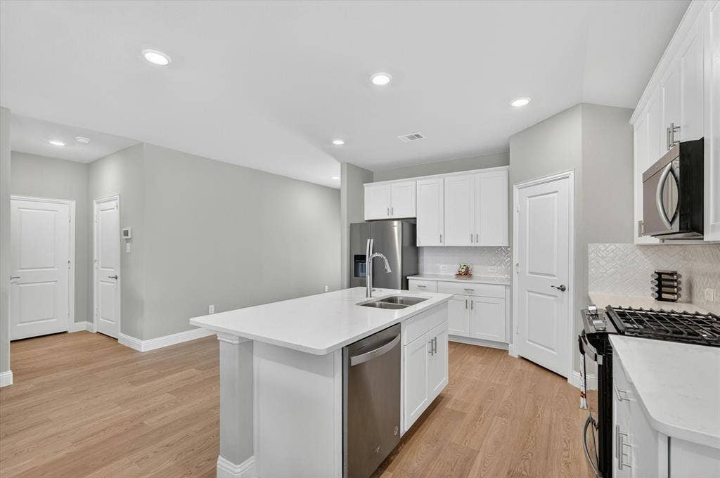 903 Edgehurst Drive, Princeton, TX 75071 Kitchen featuring a central island with an undermount sink, stainless steel appliances, white cabinetry, light countertops, and wood-finish flooring