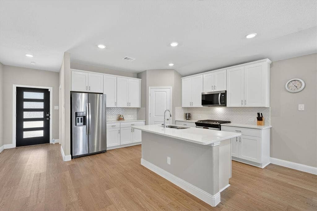 903 Edgehurst Drive, Princeton, TX 75071 Open-concept kitchen with a central island, white shaker cabinetry, stainless steel appliances, and wood-finish flooring