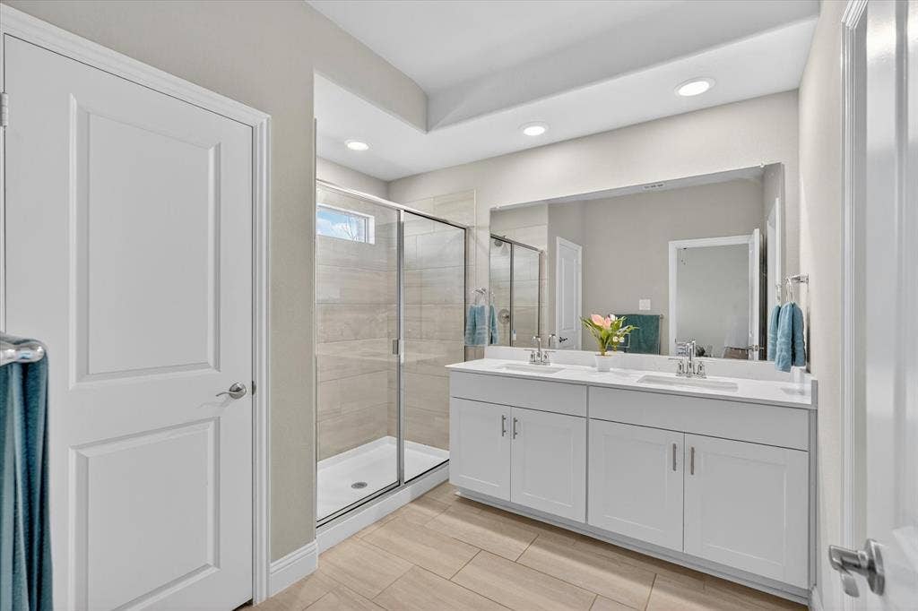 903 Edgehurst Drive, Princeton, TX 75071 Bathroom featuring a dual vanity with white cabinetry and integrated sinks, a large frameless mirror, and a glass-enclosed shower with tile surround