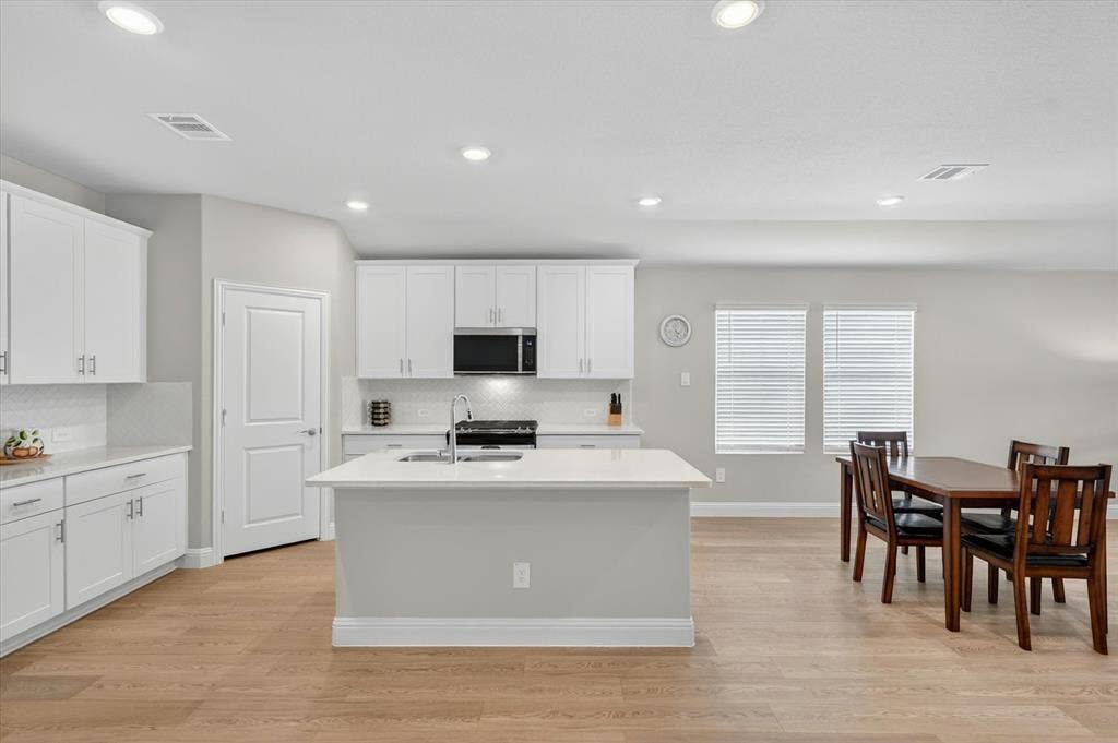 903 Edgehurst Drive, Princeton, TX 75071 Kitchen featuring white cabinetry, light-toned countertops, a central island with a sink, stainless steel appliances, and wood-finish flooring