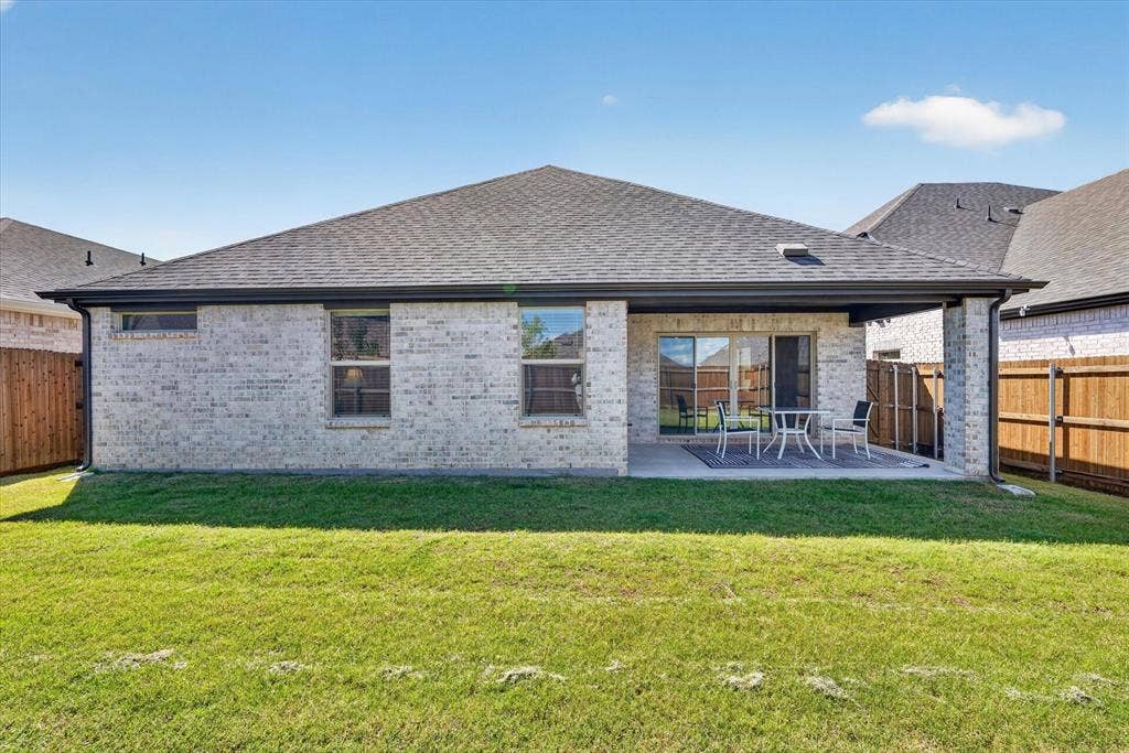 903 Edgehurst Drive, Princeton, TX 75071 Expansive backyard featuring a manicured lawn, a covered patio, and a light-colored brick exterior