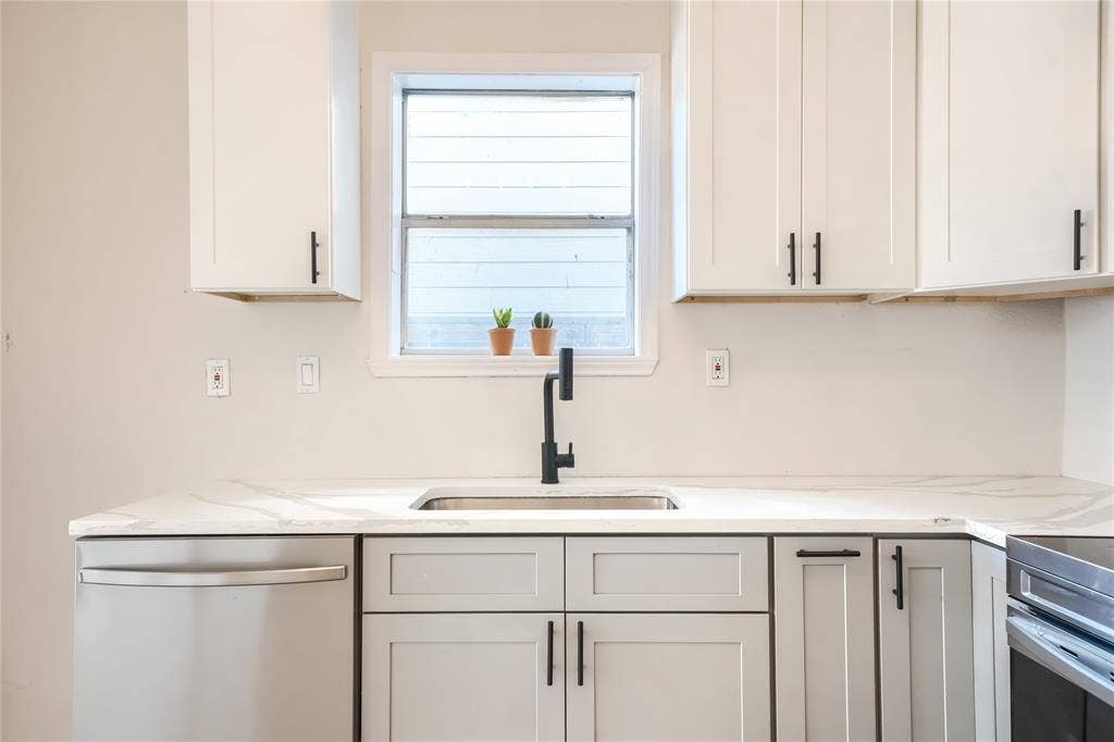 Kitchen featuring white upper cabinetry, grey lower cabinetry, stone-finish countertops, stainless steel undermount sink, and matte black hardware