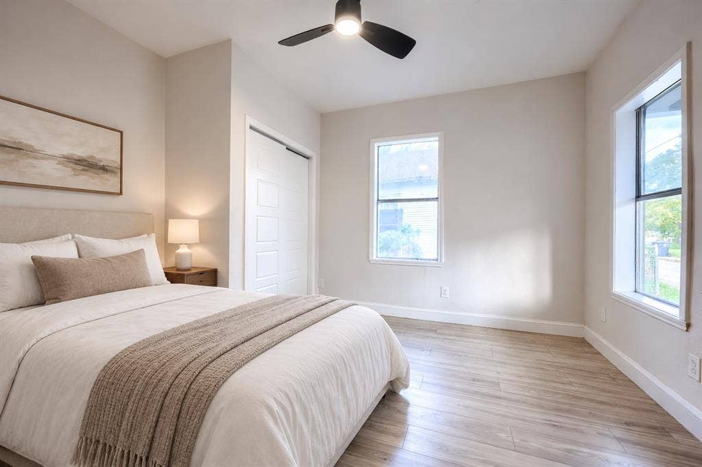 Neutral interior featuring wood-finish flooring, crisp white trim, two windows, and a matte black ceiling fan with integrated lighting