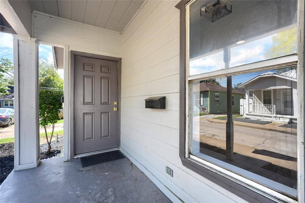 Covered entryway featuring horizontal lap siding, a paneled door, a large fixed-pane window with dark trim, and a wall-mounted metal mailbox
