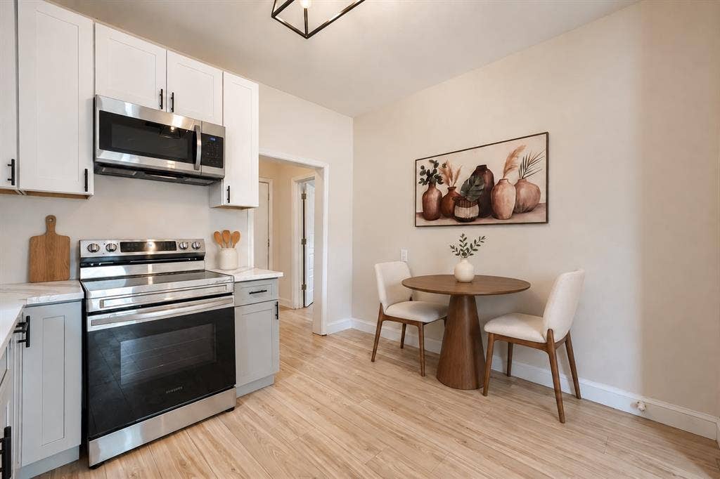 Kitchen featuring white and grey shaker-style cabinetry, stainless steel appliances, light-toned wood-finish flooring, and a modern geometric pendant light fixture