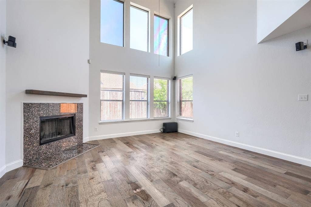 1127 Valley Vista Drive, Irving, TX 75063 Double-height living area featuring floor-to-ceiling windows, stone-surround fireplace with a timber mantel, and wood-finish flooring