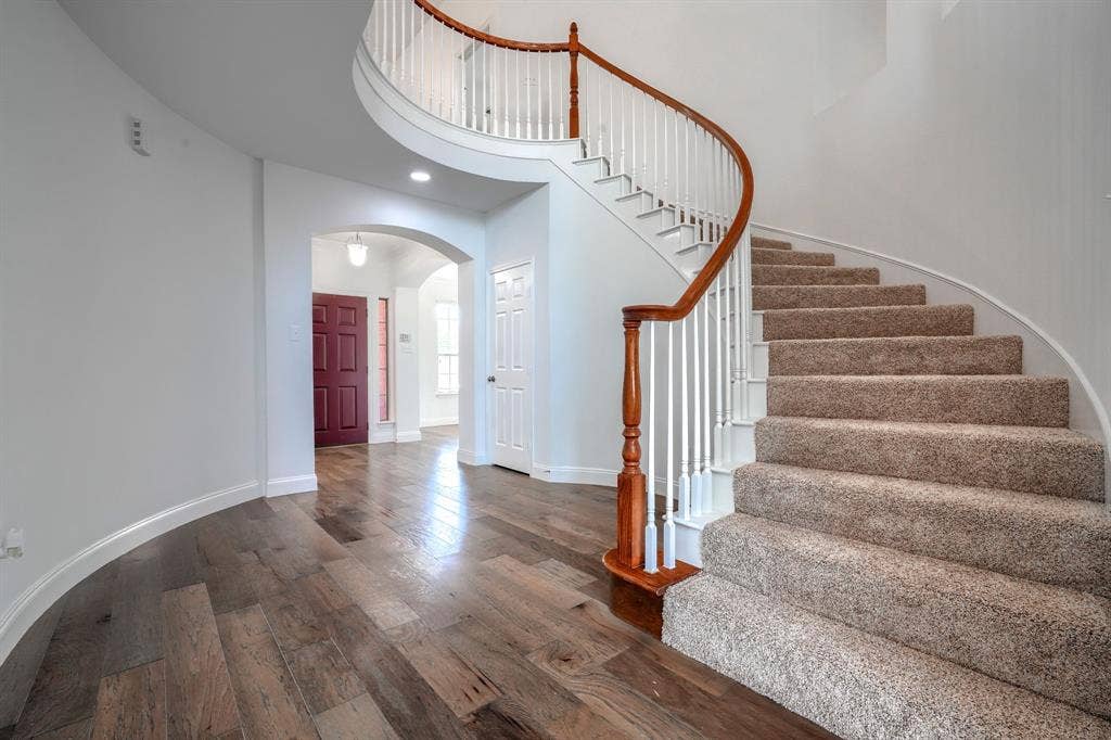 1127 Valley Vista Drive, Irving, TX 75063 Curved staircase with wood handrail, white balusters, and carpeted treads, featuring wood-finish flooring and arched entryway