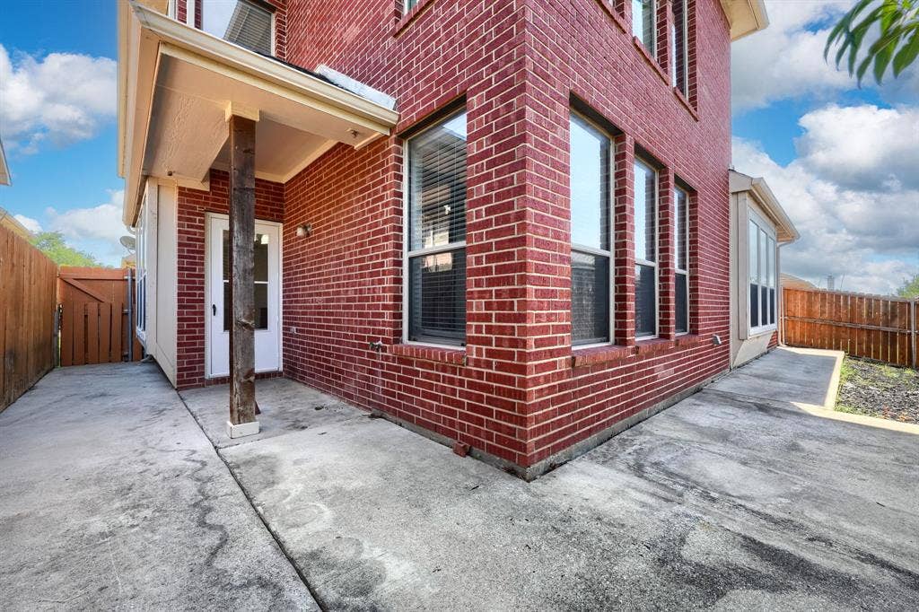 1127 Valley Vista Drive, Irving, TX 75063 Red brick exterior featuring a covered patio with a wooden support post, multiple rectangular windows, and concrete surfacing