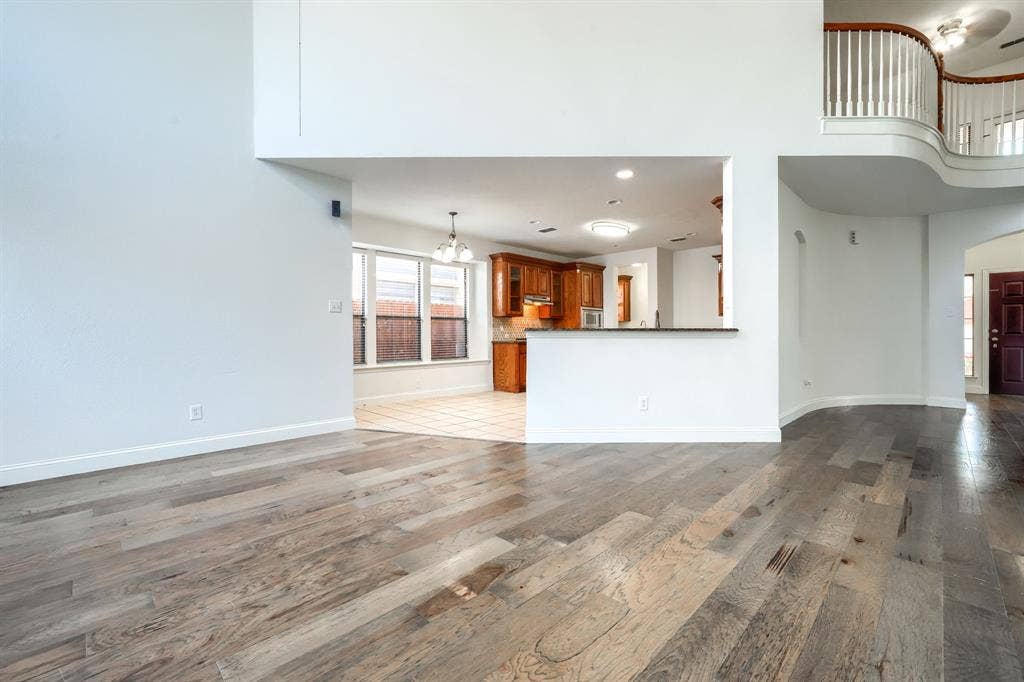 1127 Valley Vista Drive, Irving, TX 75063 High-ceiling interior featuring wood-finish flooring, a kitchen with wood cabinetry, a stone-surface breakfast bar, and a curved staircase with a spindle railing