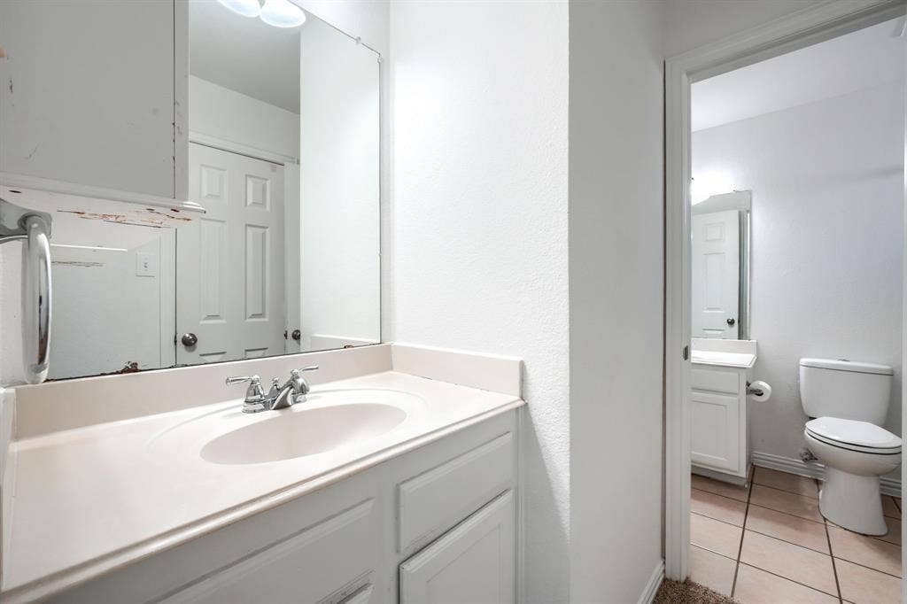 1127 Valley Vista Drive, Irving, TX 75063 Bathroom vanity featuring a solid-surface countertop with an integrated basin, chrome dual-handle faucet, large wall-mounted mirror, and white shaker-style cabinetry