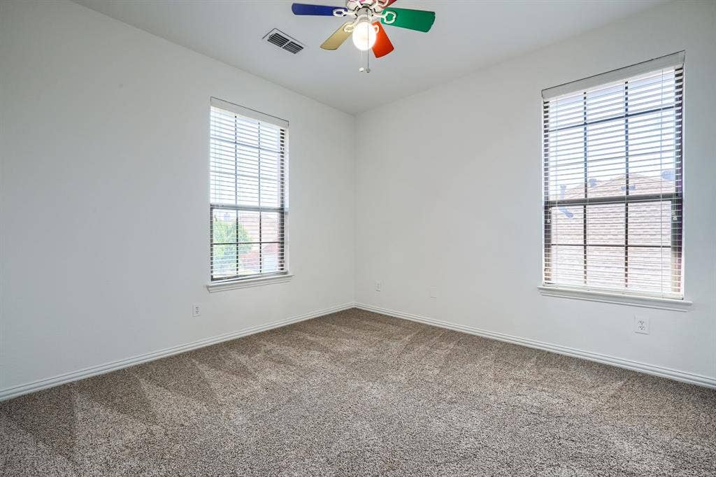 1127 Valley Vista Drive, Irving, TX 75063 Interior room featuring textured carpeting, neutral wall color, dual windows with fitted horizontal blinds, and a multi-colored ceiling fan with integrated light fixture
