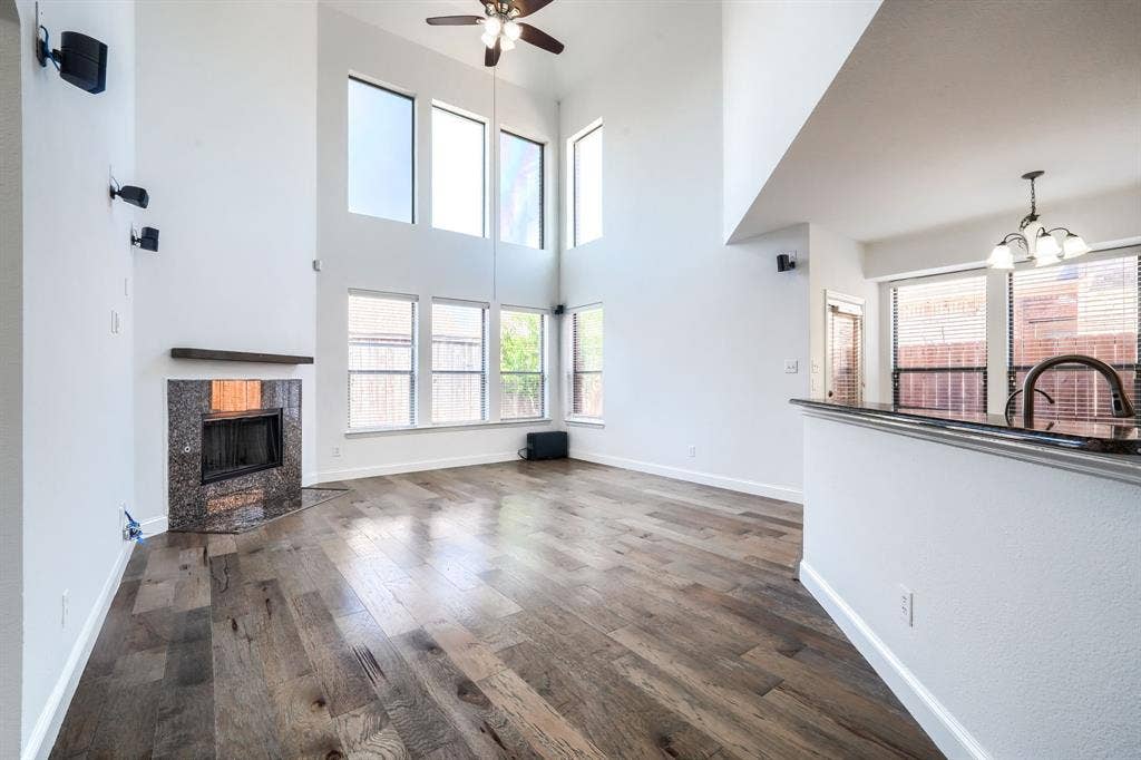 1127 Valley Vista Drive, Irving, TX 75063 Two-story ceiling with expansive windows, wood-finish flooring, fireplace with stone surround and wooden mantel, and a kitchen peninsula with stone-finish countertop