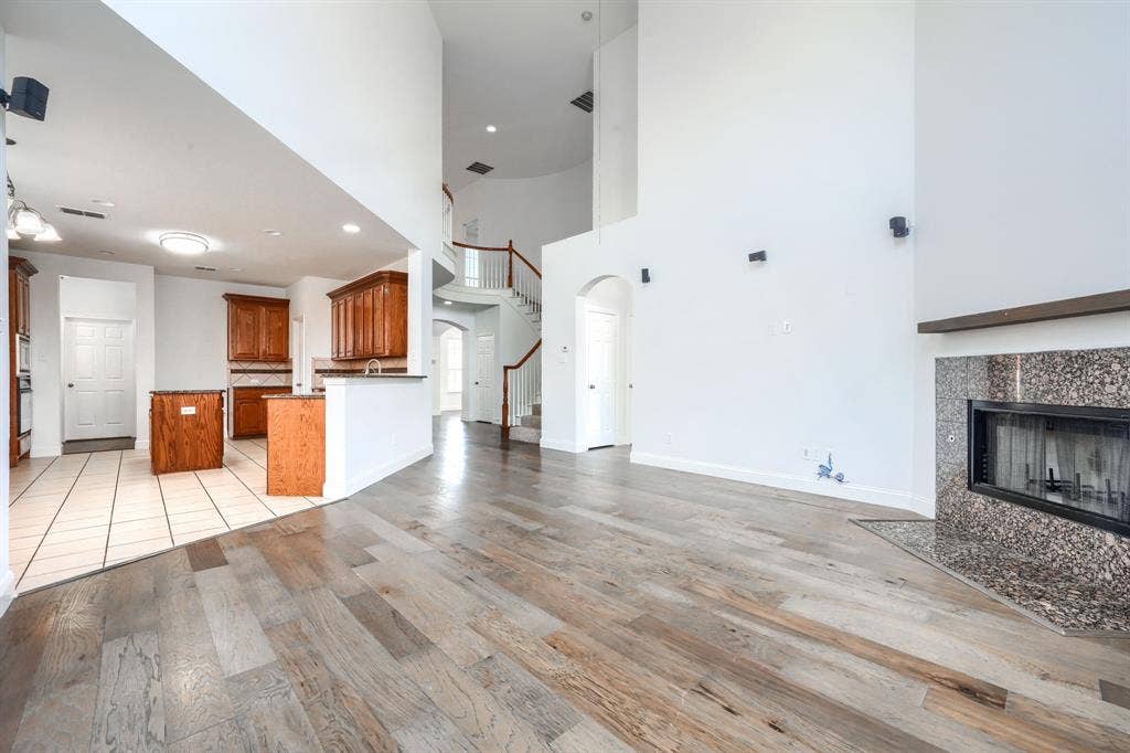 1127 Valley Vista Drive, Irving, TX 75063 High-ceiling living area featuring wood-finish flooring and a stone-surround fireplace, complemented by a kitchen with wood cabinetry, a central island, and tile flooring
