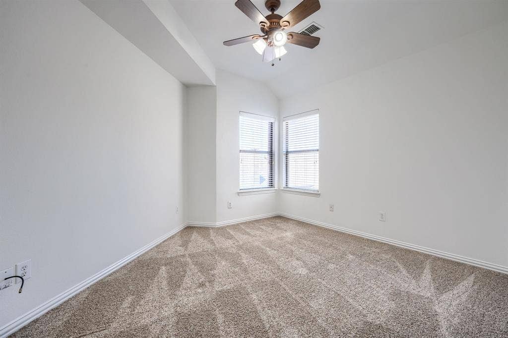 1127 Valley Vista Drive, Irving, TX 75063 Neutral-toned carpeted room featuring a vaulted ceiling, dual windows with blinds, and a ceiling fan with integrated lighting