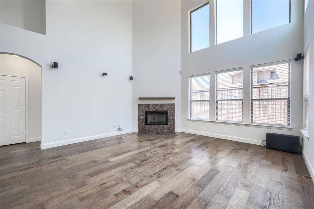 1127 Valley Vista Drive, Irving, TX 75063 Double-height ceiling, wood-finish flooring, floor-to-ceiling windows, and corner fireplace with stone surround and mantle