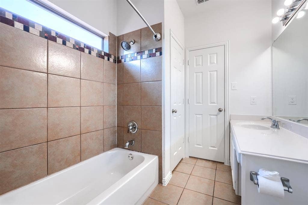 1127 Valley Vista Drive, Irving, TX 75063 Bathroom featuring a tub-shower combination with floor-to-ceiling tile surround, decorative mosaic tile accent, clerestory window, white vanity cabinet with solid surface countertop, and tile flooring