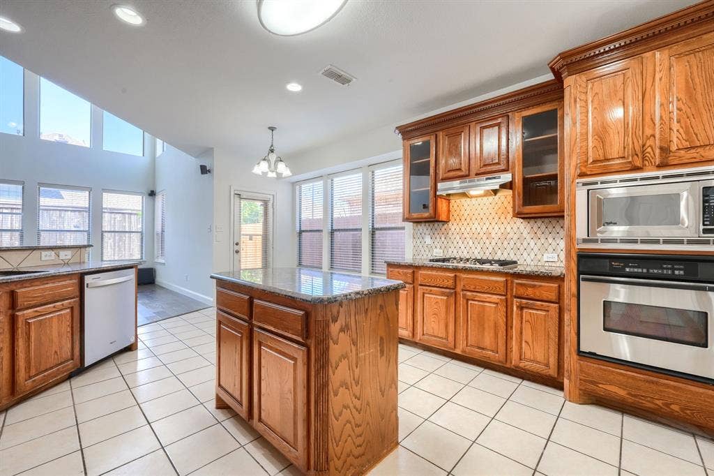 1127 Valley Vista Drive, Irving, TX 75063 Kitchen featuring wood cabinetry, stone countertops, a center island, stainless steel built-in appliances, and tile flooring