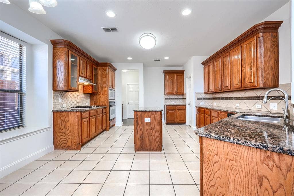 1127 Valley Vista Drive, Irving, TX 75063 Kitchen featuring stained wood cabinetry, stone countertops, a central island, tiled flooring, and a decorative tile backsplash