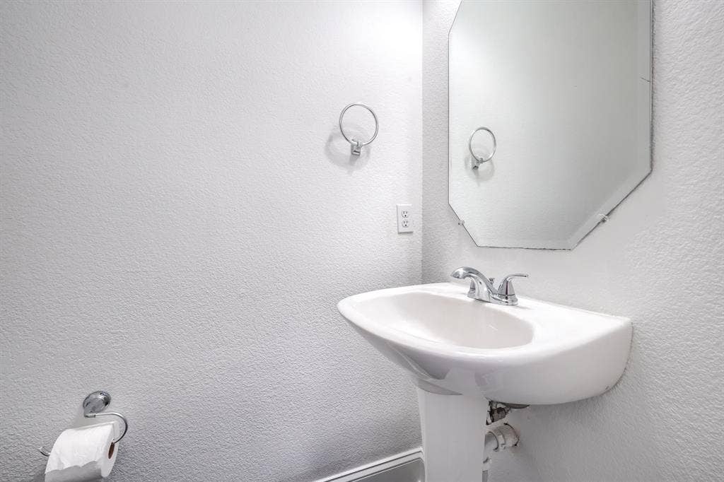 1127 Valley Vista Drive, Irving, TX 75063 Wall-mounted pedestal sink with a polished chrome dual-handle faucet, octagonal mirror, and attached circular towel ring