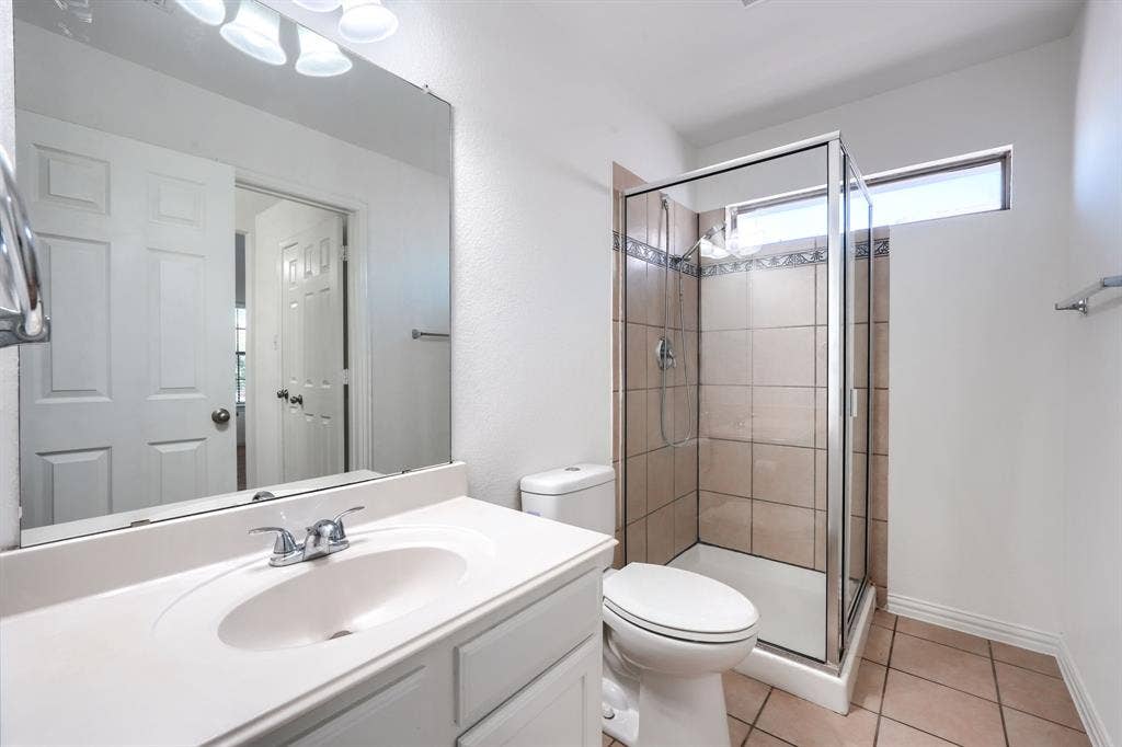1127 Valley Vista Drive, Irving, TX 75063 Bathroom featuring a vanity with an integrated sink, large wall-mounted mirror, glass-enclosed shower with tile surround, and tile flooring