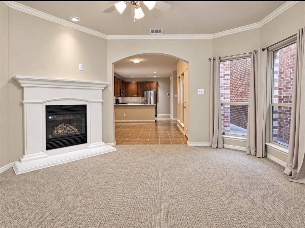 2002 Downing Street, Allen, TX 75013 Living area featuring a white fireplace mantle with a central hearth, crown molding, arched entry, and large windows with natural light