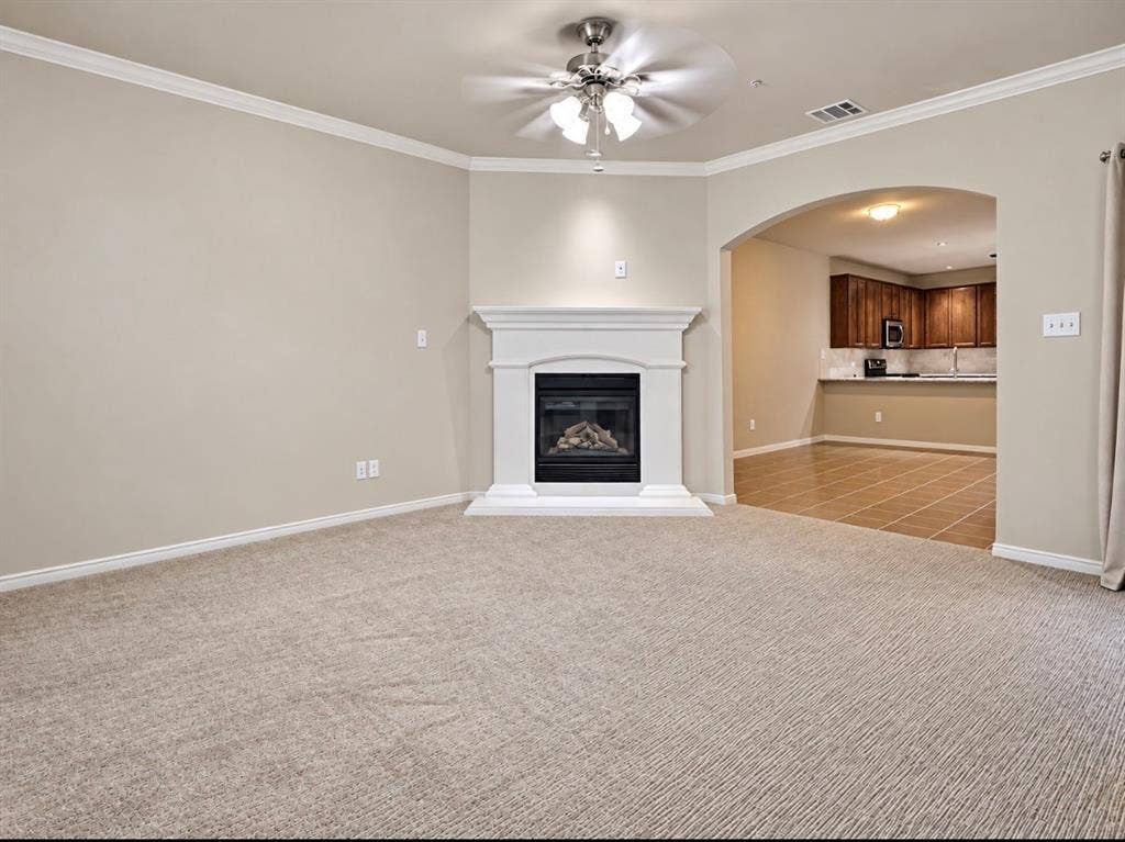 2002 Downing Street, Allen, TX 75013 Living area featuring crown molding, a central fireplace with a white mantel, an arched entry, and a ceiling fan with integrated lighting