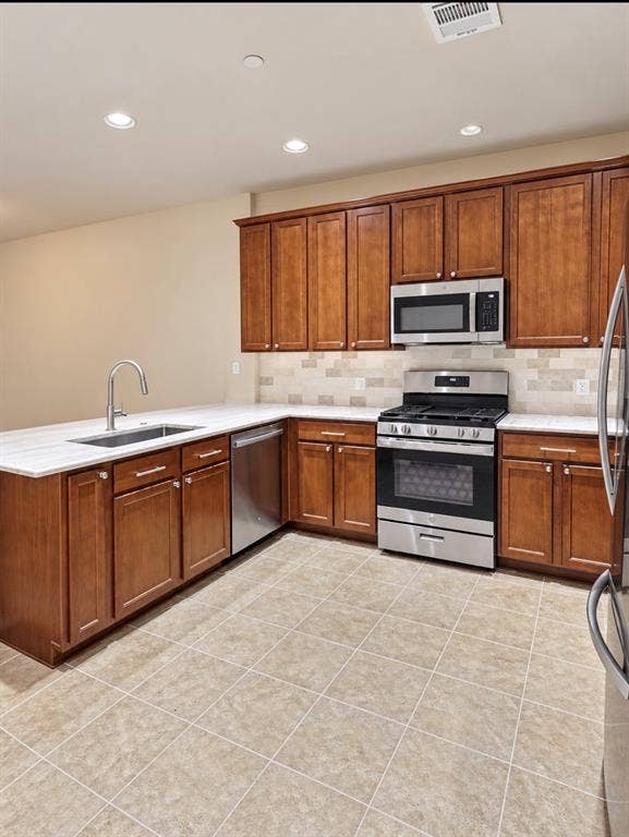 2002 Downing Street, Allen, TX 75013 Kitchen featuring shaker-style wood cabinetry, stainless steel appliances, light-toned stone-finish countertops, tiled backsplash, and recessed lighting