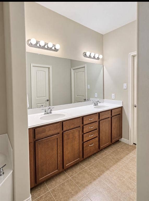 2002 Downing Street, Allen, TX 75013 Double vanity featuring stained wood cabinetry, a solid-surface countertop, dual drop-in sinks, polished chrome faucets, and full-width wall mirror with integrated vanity lighting