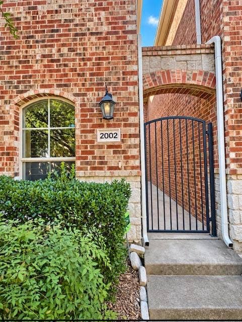 2002 Downing Street, Allen, TX 75013 Brick exterior featuring a stone base, arched window with decorative muntins, wrought iron gate, and wall-mounted exterior sconce