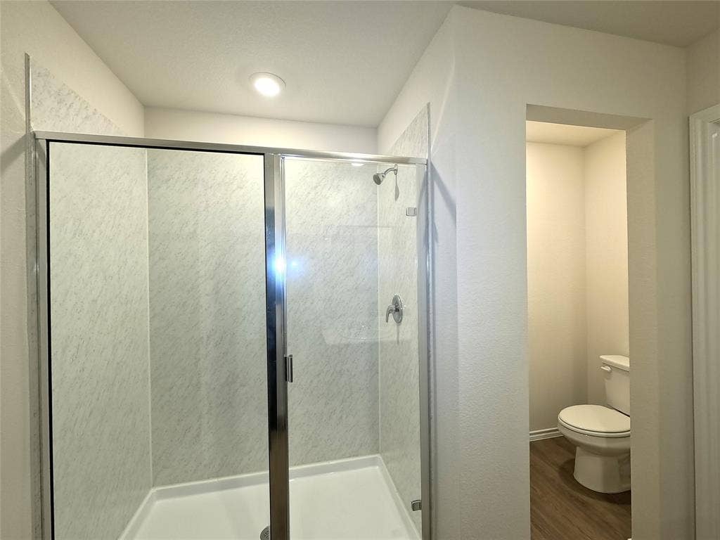 4017 Bronco Drive, Princeton, TX 75407 Shower stall featuring a glass enclosure with chrome trim and stone-patterned surround, recessed lighting, and wood-finish flooring