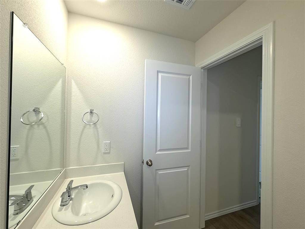 4017 Bronco Drive, Princeton, TX 75407 Vanity featuring an oval drop-in sink, solid-surface countertop, full-width wall mirror, and chrome dual-handle faucet