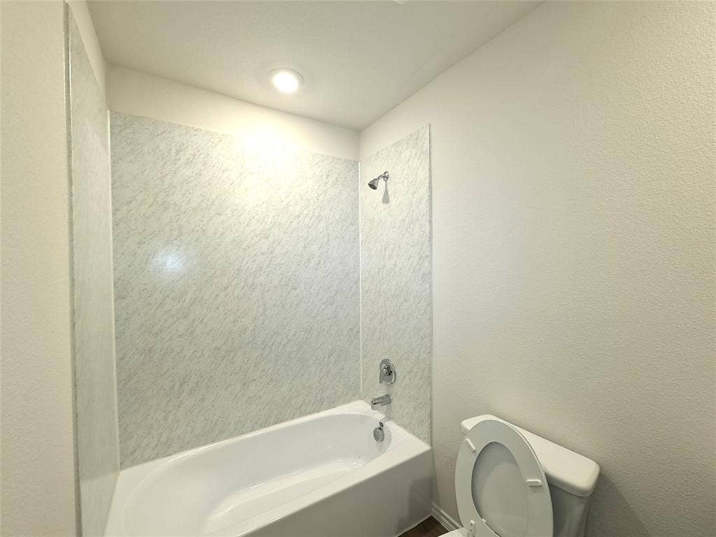 4017 Bronco Drive, Princeton, TX 75407 Bathroom featuring a white soaking tub with stone-patterned wall surround, polished chrome shower head and faucet hardware, and recessed ceiling lighting