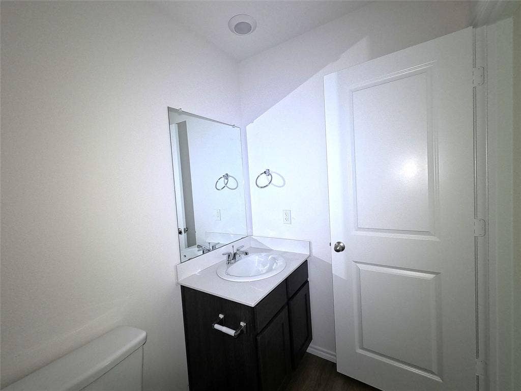 4017 Bronco Drive, Princeton, TX 75407 Vanity cabinet with dark wood-finish cabinetry, white countertop, integrated basin, wall-mounted mirror, and chrome hardware