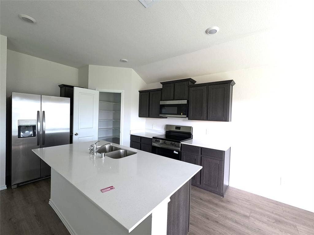 4017 Bronco Drive, Princeton, TX 75407 Kitchen featuring dark wood-finish cabinetry, quartz countertops, a central island with a double-basin stainless steel sink, stainless steel appliances, and a walk-in pantry
