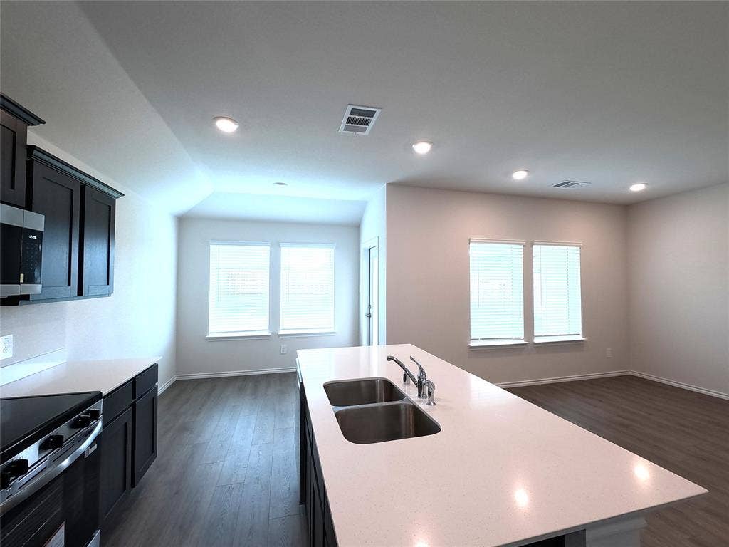 4017 Bronco Drive, Princeton, TX 75407 Kitchen featuring dark cabinetry, expansive center island with stone-finish countertop, dual-basin stainless steel sink, and wood-finish flooring