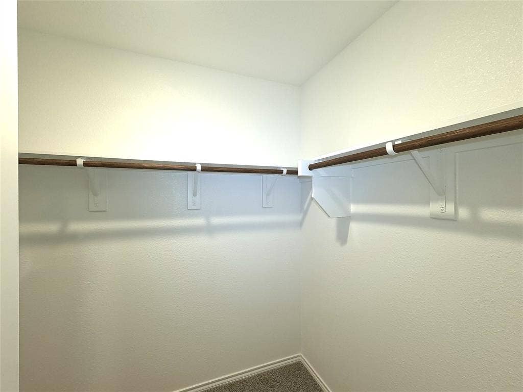 4017 Bronco Drive, Princeton, TX 75407 Storage area featuring wrap-around wooden garment rods, white painted shelving, and neutral carpeting