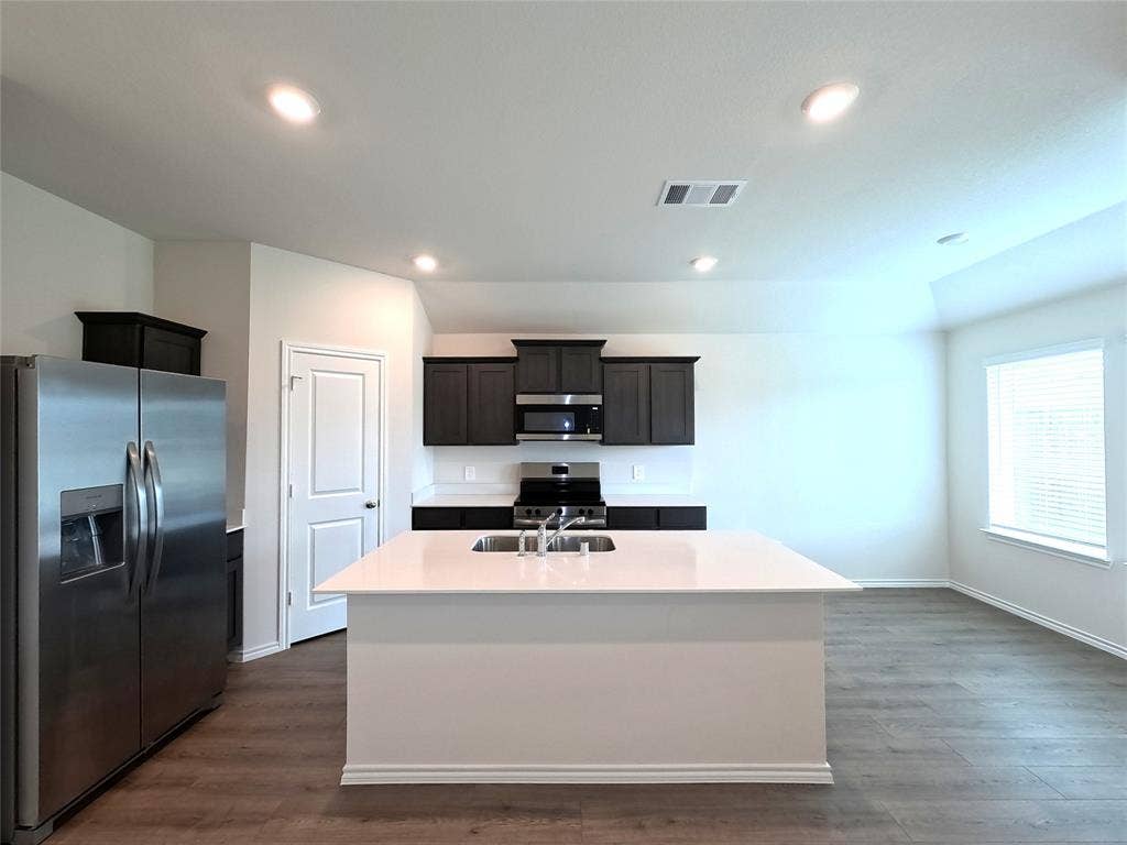 4017 Bronco Drive, Princeton, TX 75407 Kitchen featuring a center island with a solid surface countertop, dark cabinetry, stainless steel appliances, and wood-finish flooring