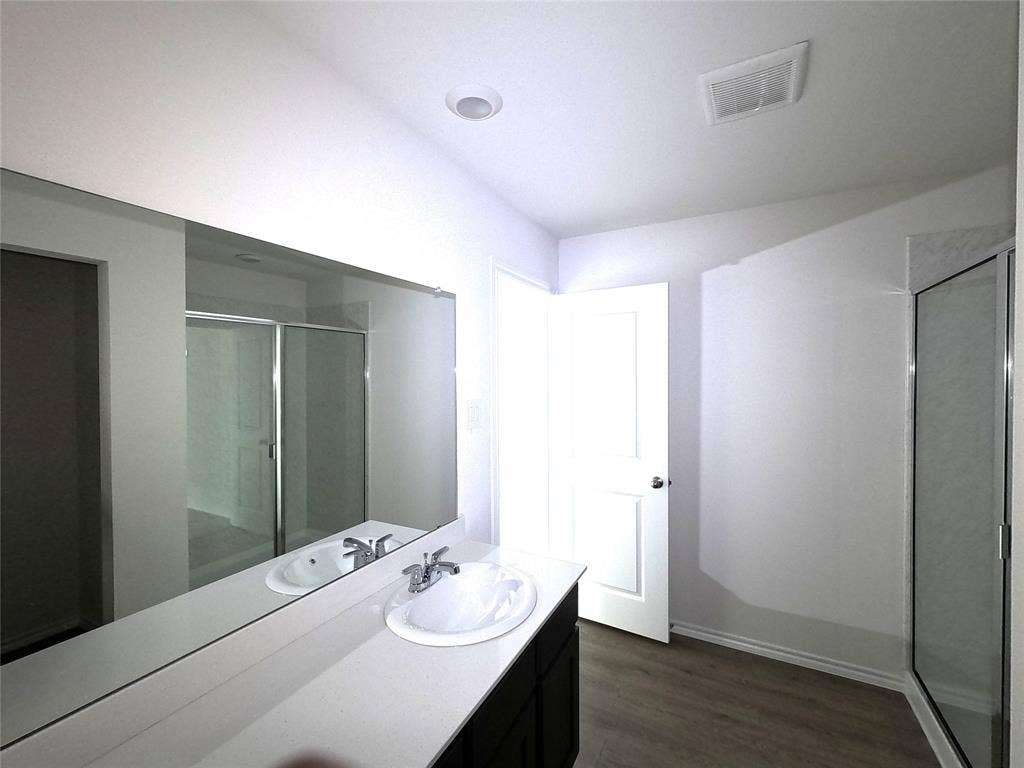 4017 Bronco Drive, Princeton, TX 75407 Bathroom featuring a white vanity with a composite countertop, undermount sink, chrome faucet, expansive wall mirror, and a glass-enclosed shower