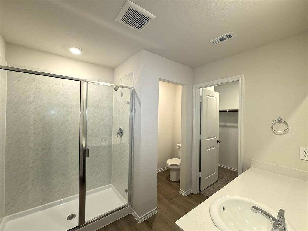 4017 Bronco Drive, Princeton, TX 75407 Walk-in shower with a glass enclosure, solid-surface countertop with an integrated sink, wood-finish flooring, and a separate water closet area