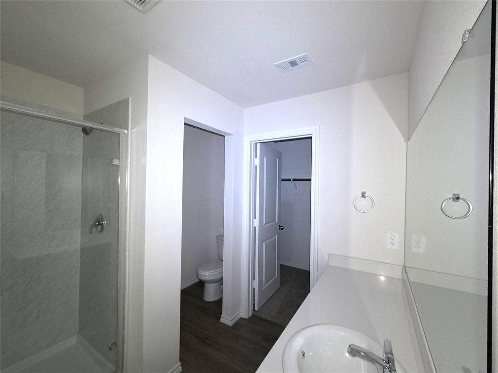 4017 Bronco Drive, Princeton, TX 75407 Full-width wall mirror, shower with glass enclosure and surround, solid-surface countertop with integrated basin, and neutral-tone flooring