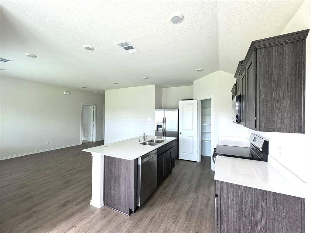 4017 Bronco Drive, Princeton, TX 75407 Kitchen featuring dark-finish cabinetry, quartz countertops, central island with an integrated stainless steel dual-basin sink, stainless steel appliances, and wood-finish flooring