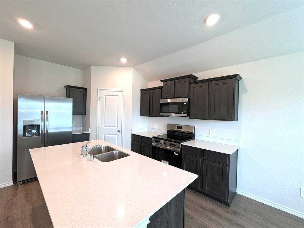 4017 Bronco Drive, Princeton, TX 75407 Kitchen featuring dark cabinetry, solid-surface countertops, center island with an undermount double-basin sink, and stainless steel appliances